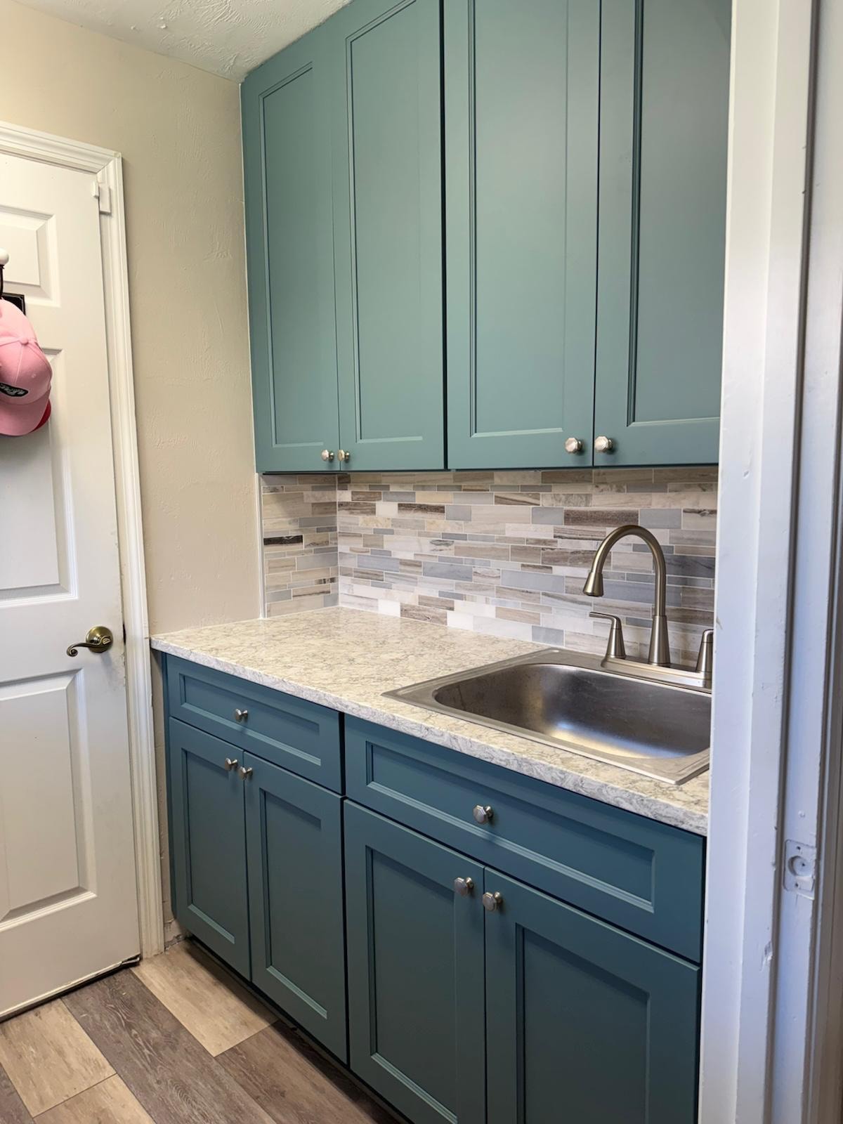 Remodeled kitchen with teal cabinetry, tile backsplash, and stainless-steel sink